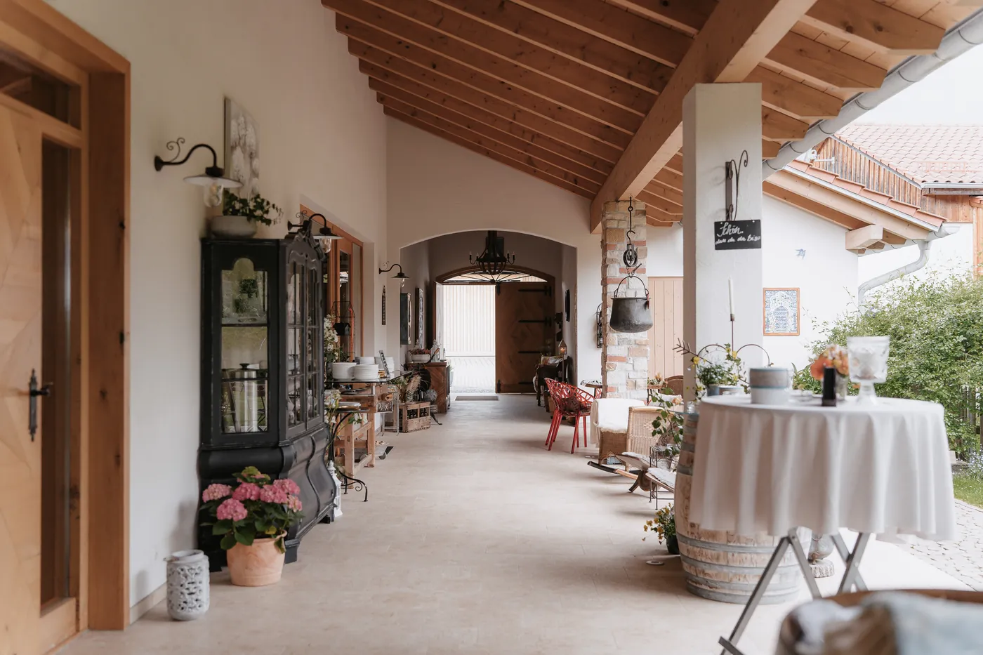 Bayerisch-italienisches Ambiente im überdachten Gang des Hof Nr. 6 mit Holzbalkendecke, Stehtisch und mediterranen Details
