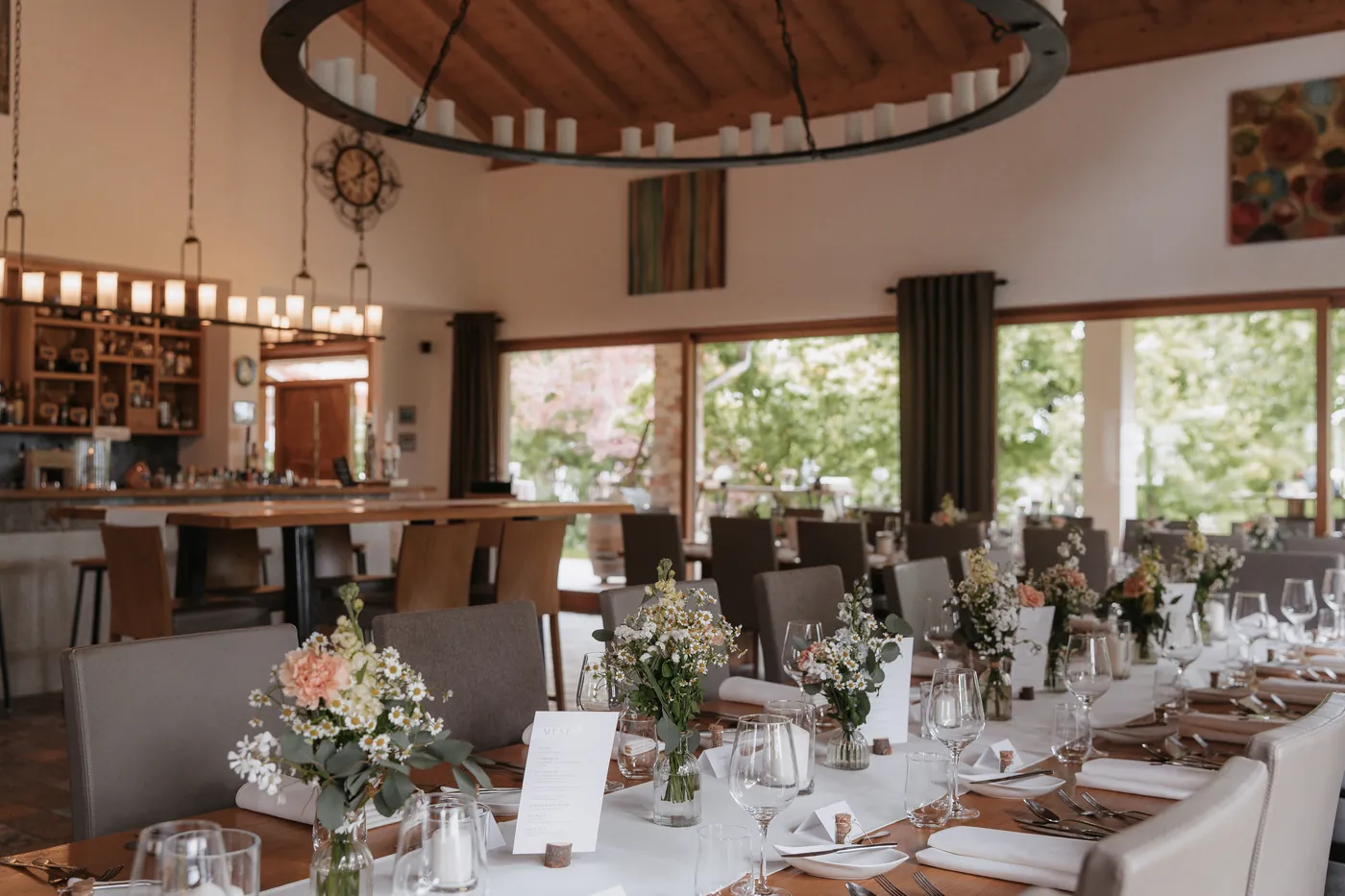 Festlich eingedeckte Hochzeitstafel im Hauptraum des Hof Nr. 6 mit Blumenschmuck, rundem Kerzenleuchter und Blick ins Grüne