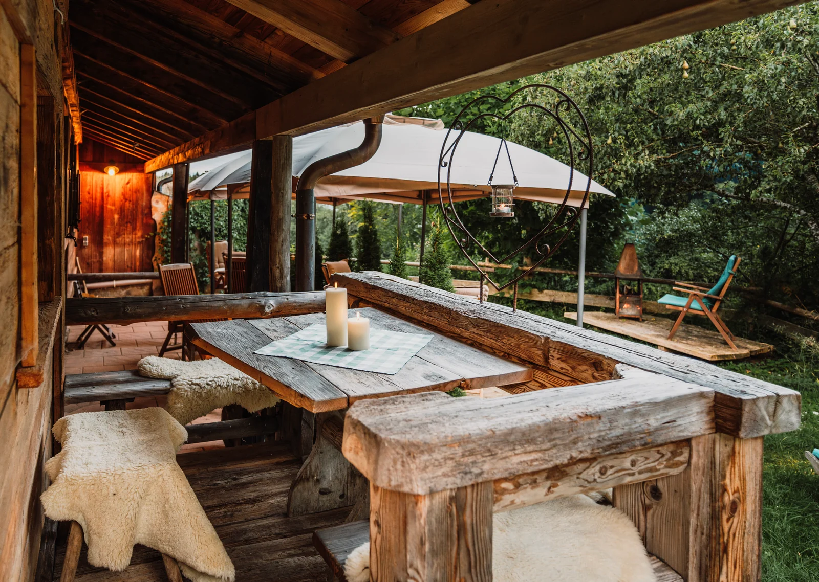 Überdachte Terrasse mit Altholztisch, Kerzen, Schaffellen und Herzlaterne am Chalet der Edelsberghütte